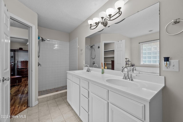 bathroom with tile patterned flooring, vanity, tiled shower, and a textured ceiling