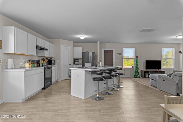 kitchen with white cabinets, a kitchen island with sink, stainless steel appliances, and light wood-type flooring