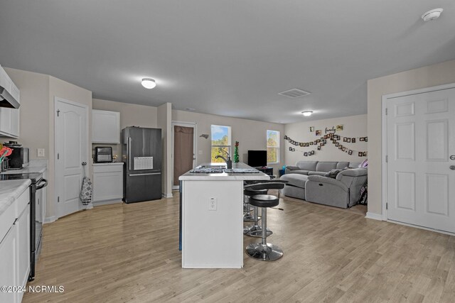 kitchen with a kitchen bar, a kitchen island, stainless steel fridge, white cabinets, and black / electric stove