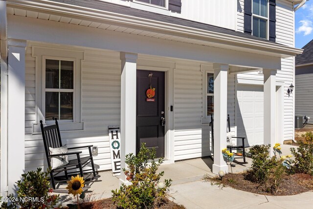 view of exterior entry featuring central AC, covered porch, and a garage