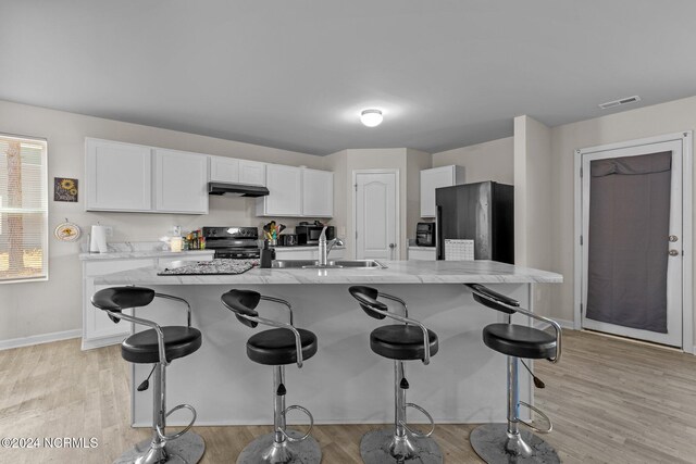 kitchen featuring an island with sink, black appliances, a breakfast bar, light wood-type flooring, and white cabinetry