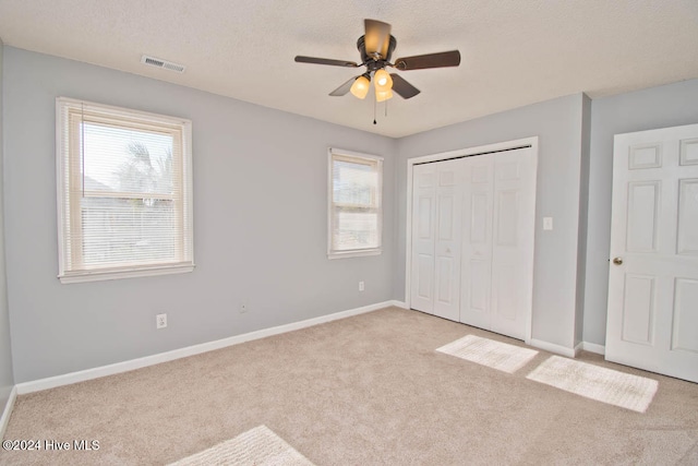 unfurnished bedroom featuring a textured ceiling, ceiling fan, light carpet, and a closet