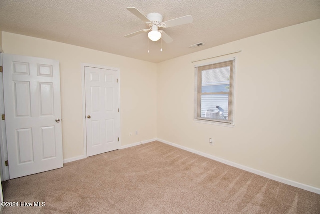 unfurnished bedroom featuring light carpet, a textured ceiling, and ceiling fan