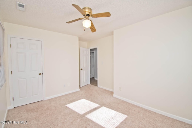 unfurnished bedroom with ceiling fan, light carpet, and a textured ceiling