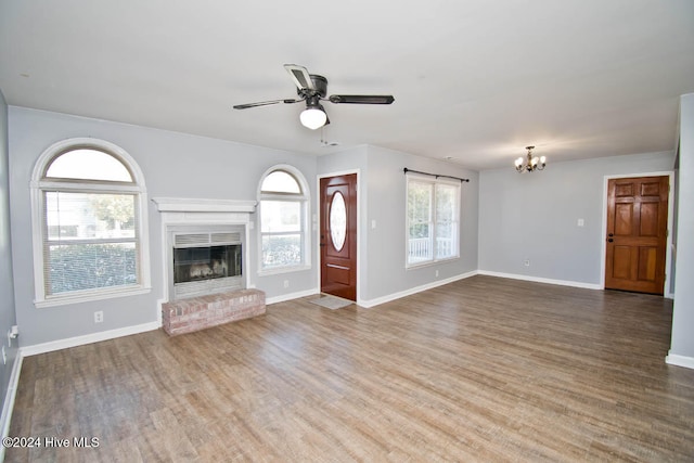 unfurnished living room with ceiling fan with notable chandelier, hardwood / wood-style flooring, and a brick fireplace