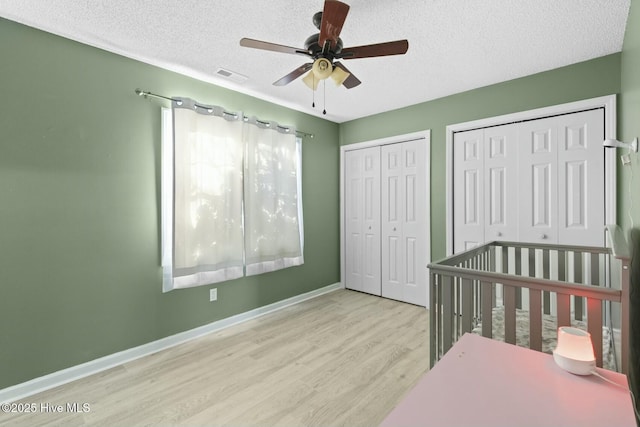 bedroom with light wood-type flooring, ceiling fan, a textured ceiling, and multiple closets