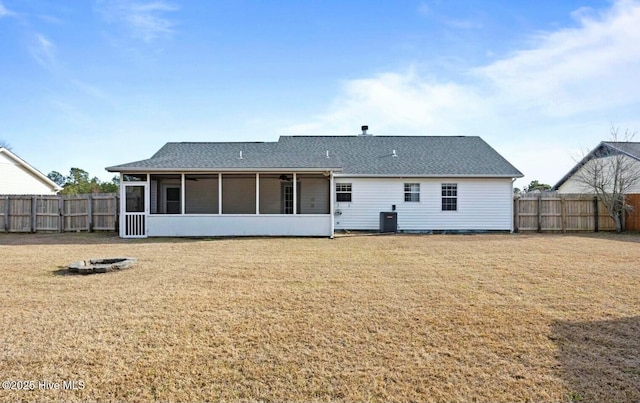 rear view of house with a sunroom, cooling unit, a lawn, and a fire pit