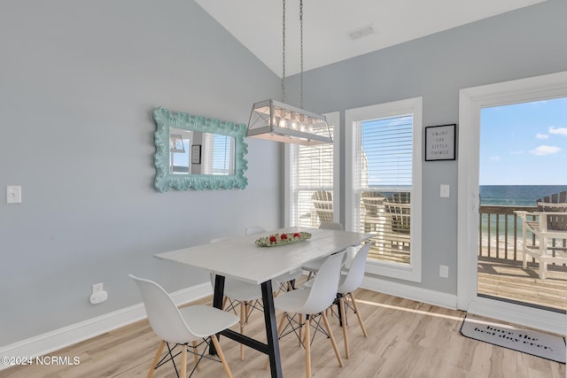 dining area with light hardwood / wood-style floors, high vaulted ceiling, and a water view