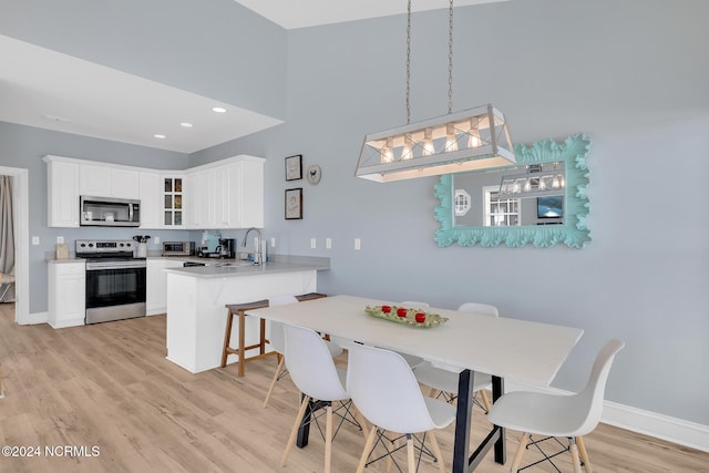 dining room with a towering ceiling, sink, and light hardwood / wood-style floors