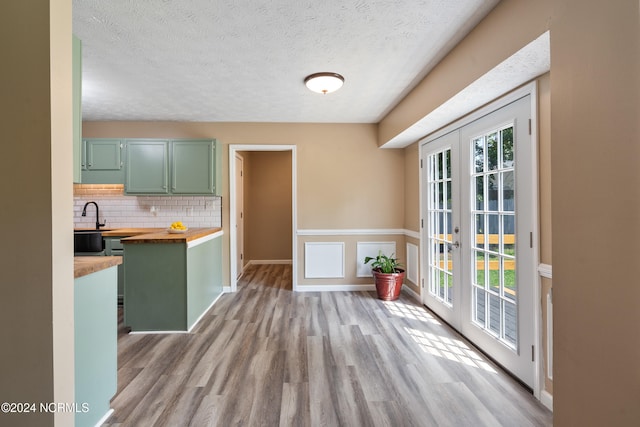 kitchen featuring french doors, butcher block counters, light hardwood / wood-style flooring, green cabinets, and backsplash