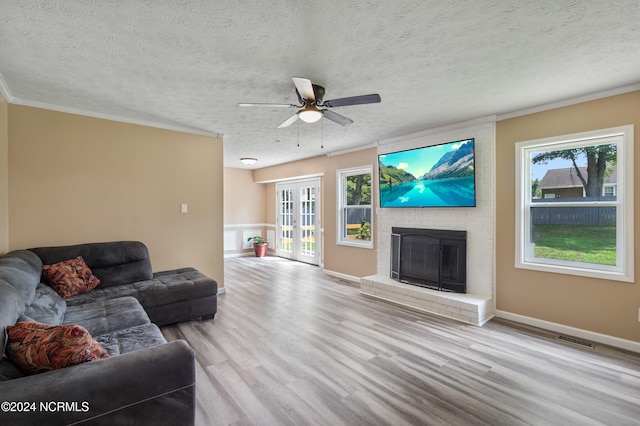 living room featuring light hardwood / wood-style floors, crown molding, a textured ceiling, and a brick fireplace