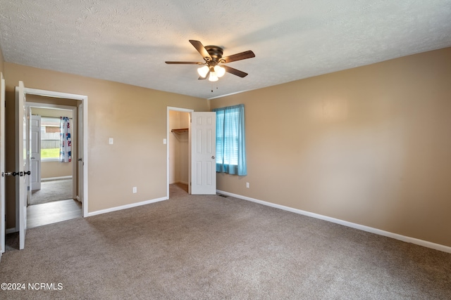 unfurnished bedroom with a closet, a walk in closet, carpet flooring, a textured ceiling, and ceiling fan