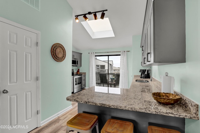 kitchen featuring gray cabinetry, stainless steel appliances, sink, light wood-type flooring, and lofted ceiling with skylight