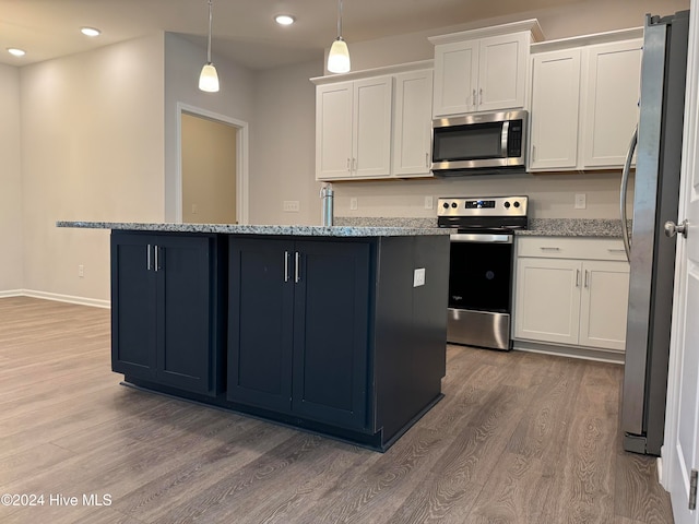 kitchen featuring a center island with sink, hardwood / wood-style floors, decorative light fixtures, white cabinetry, and appliances with stainless steel finishes