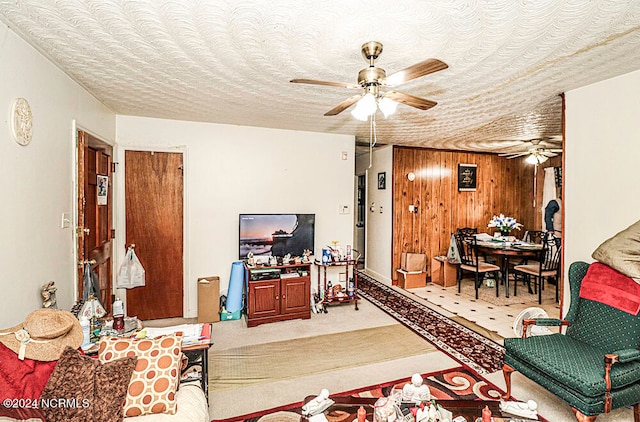 living room featuring ceiling fan, wood walls, and a textured ceiling