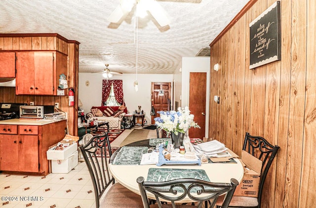 dining space with ceiling fan, a textured ceiling, and wooden walls