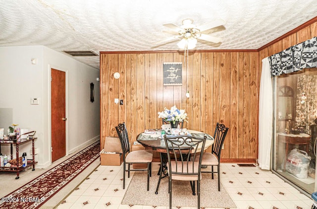 dining room featuring ceiling fan, crown molding, a textured ceiling, and wooden walls