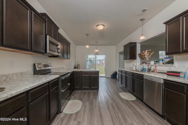 kitchen featuring light wood-type flooring, appliances with stainless steel finishes, decorative light fixtures, and a textured ceiling