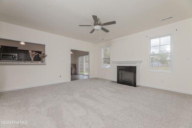 unfurnished living room featuring a textured ceiling, a wealth of natural light, ceiling fan, and light colored carpet