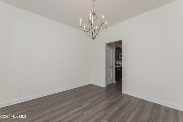 unfurnished room featuring dark wood-type flooring and an inviting chandelier