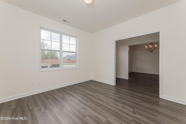 spare room featuring dark wood-type flooring and an inviting chandelier