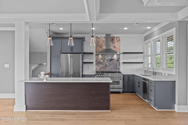 kitchen with high end appliances, wall chimney exhaust hood, sink, pendant lighting, and light wood-type flooring