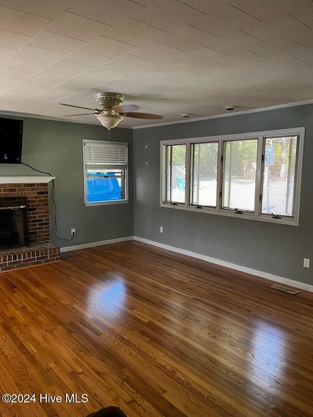 unfurnished living room featuring crown molding, a brick fireplace, wood-type flooring, and ceiling fan