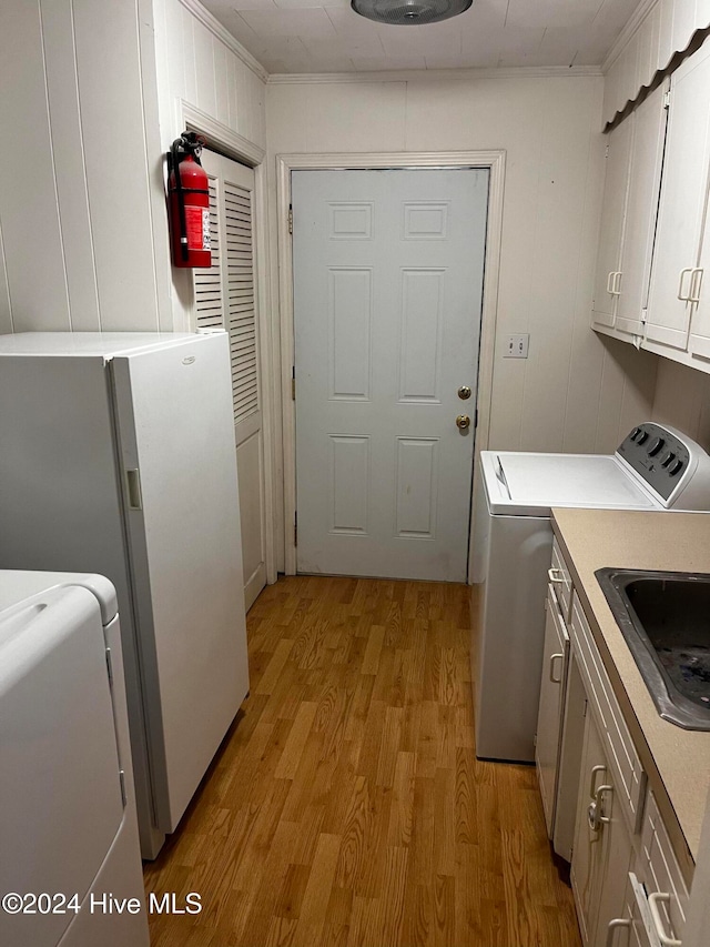 laundry room with cabinets, light wood-type flooring, ornamental molding, washing machine and dryer, and sink