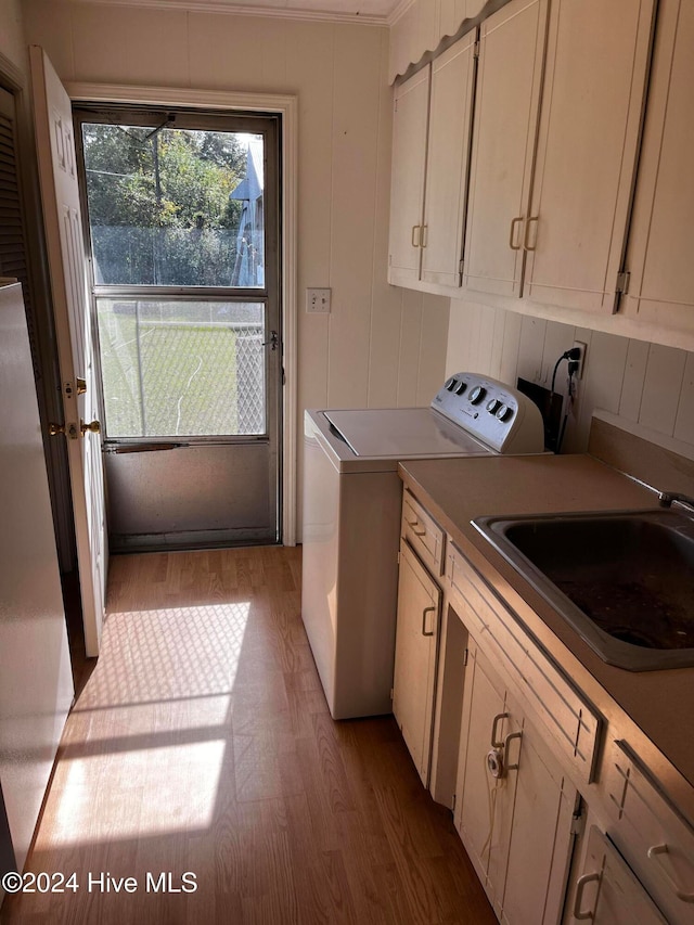 laundry area with cabinets, washing machine and clothes dryer, light hardwood / wood-style flooring, crown molding, and sink