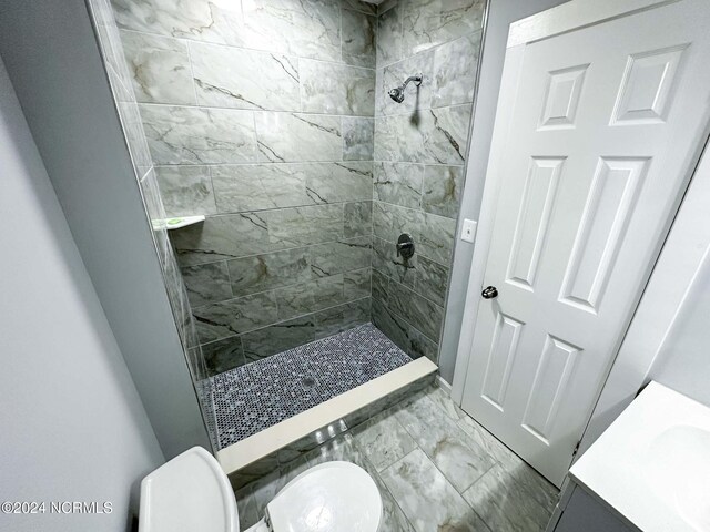 bathroom featuring a tile shower, toilet, and vanity