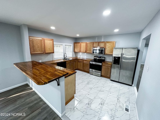 kitchen with kitchen peninsula, sink, a breakfast bar, appliances with stainless steel finishes, and tasteful backsplash