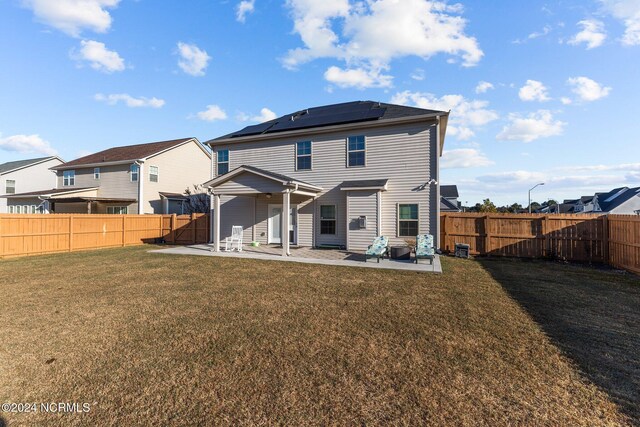 rear view of property with a patio area, a lawn, and solar panels