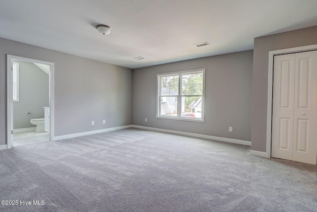 unfurnished bedroom featuring ensuite bathroom, a closet, light colored carpet, baseboards, and visible vents