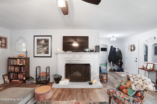 living room featuring light wood-type flooring, ceiling fan, and a brick fireplace