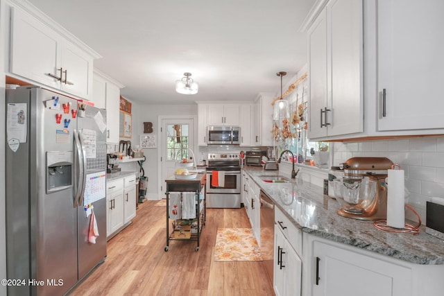 kitchen featuring white cabinets, stainless steel appliances, light hardwood / wood-style floors, and pendant lighting