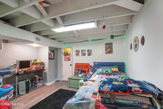 bedroom featuring brick wall and light hardwood / wood-style flooring