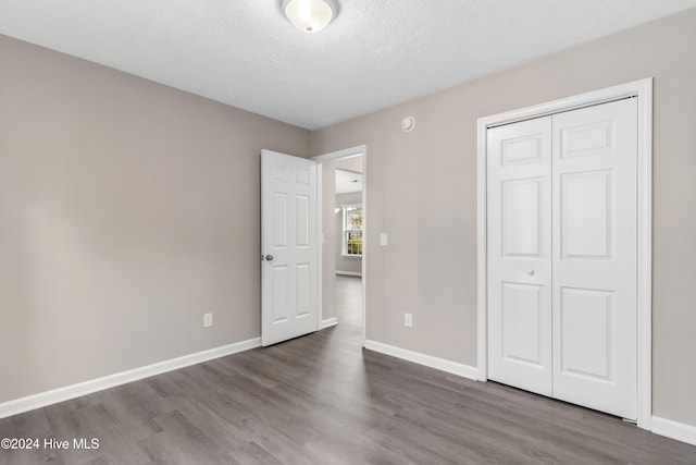 unfurnished bedroom featuring a textured ceiling, dark hardwood / wood-style flooring, and a closet