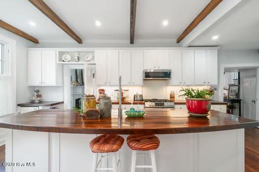 kitchen featuring white cabinetry, stainless steel appliances, a large island with sink, and beam ceiling