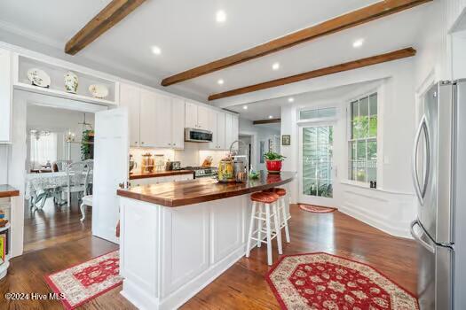 kitchen with butcher block counters, white cabinetry, appliances with stainless steel finishes, dark hardwood / wood-style floors, and beam ceiling