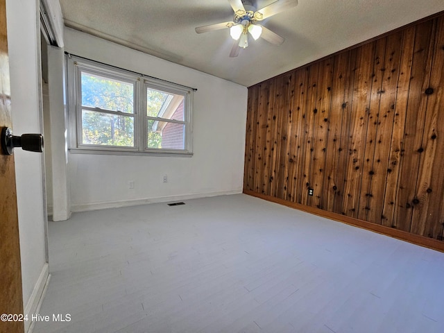 spare room featuring light hardwood / wood-style flooring, a textured ceiling, wooden walls, and ceiling fan