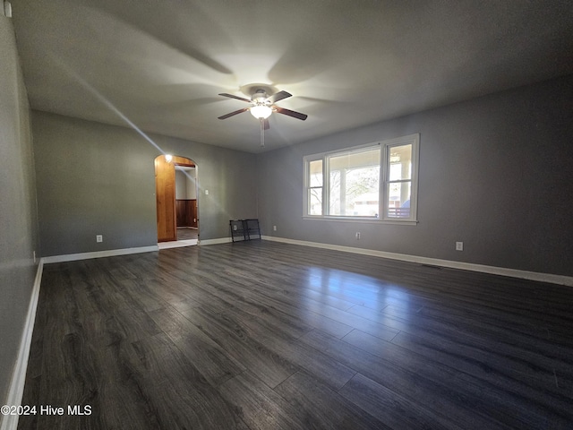 unfurnished living room with arched walkways, dark wood-style floors, baseboards, and ceiling fan