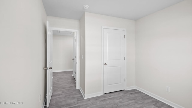 unfurnished bedroom featuring attic access, baseboards, and wood finished floors