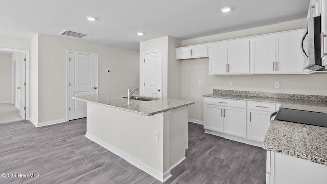 kitchen with white cabinets, stainless steel microwave, wood finished floors, light stone countertops, and a sink