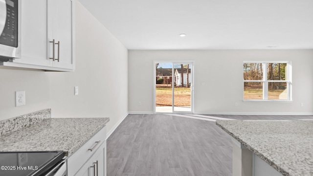 kitchen featuring light stone counters, stainless steel appliances, white cabinetry, wood finished floors, and baseboards