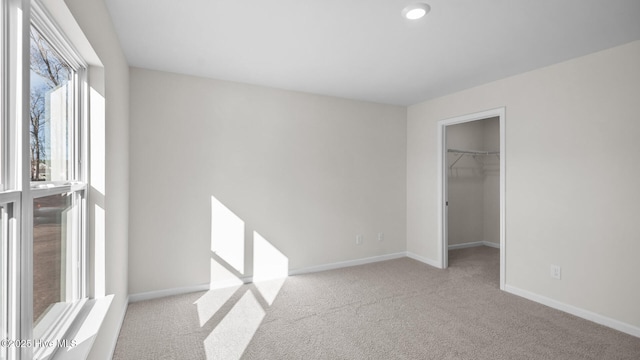 unfurnished bedroom with carpet floors, a closet, a walk in closet, and baseboards