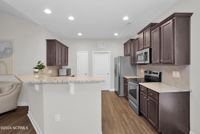 6639 Ramsey St, Fayetteville, NC 28311 - kitchen featuring appliances with stainless steel finishes, wood finished floors, dark brown cabinets, a breakfast bar area, and tasteful backsplash