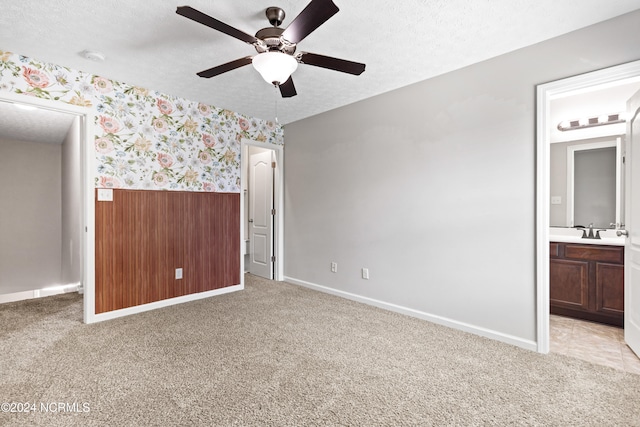 unfurnished bedroom with a textured ceiling, connected bathroom, and light carpet