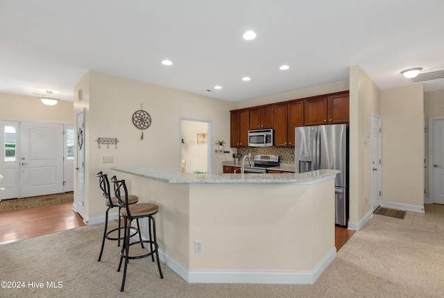 kitchen with a breakfast bar, decorative backsplash, light stone countertops, stainless steel appliances, and light carpet