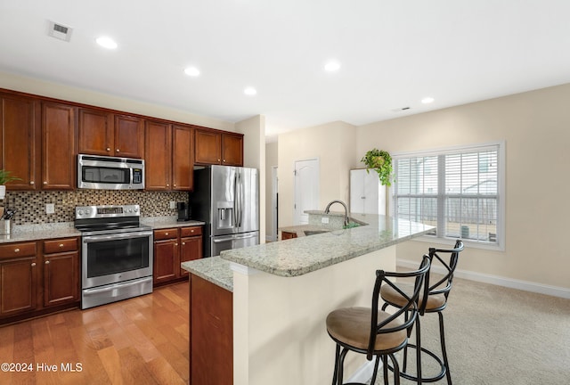 kitchen with backsplash, a kitchen bar, a kitchen island with sink, stainless steel appliances, and light stone counters