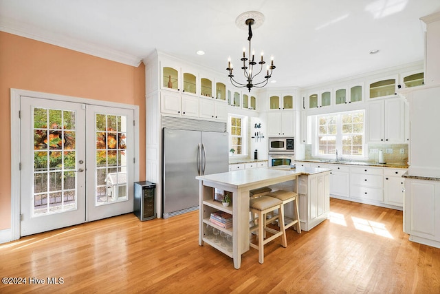 kitchen with a kitchen island, built in appliances, pendant lighting, an inviting chandelier, and light hardwood / wood-style flooring